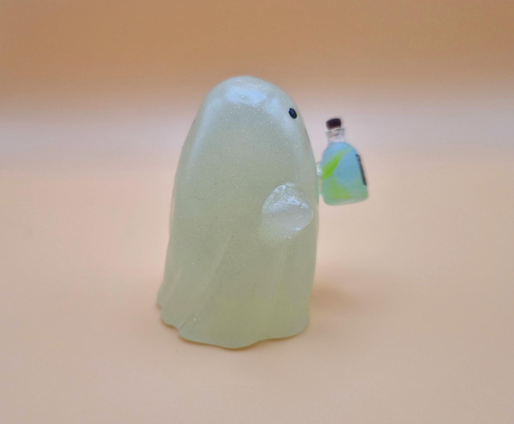 Cute night glow ghost with little blue and green poison bottle with skull on it on orange background side view